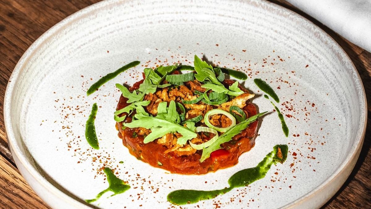 Un tartare relevé d’herbes fraîches et de rondelles d’oignon, dressé dans une assiette creuse blanche au restaurant L’Arsenic à Lyon Un tartare relevé d’herbes fraîches et de rondelles d’oignon, dressé dans une assiette creuse blanche au restaurant L’Arsenic à Lyon