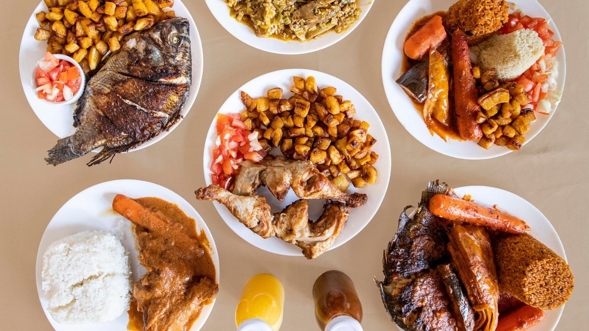 Une table de plats africains vus du dessus chez Awani, à Lyon : poisson grillé, alloco, viandes et sauces