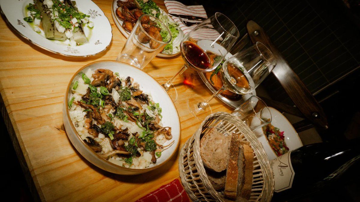 Une table en bois garnie de plats à partager, d’un risotto aux champignons, de verres de vin et d’un panier de pain, chez Bambane, bistro à Lyon