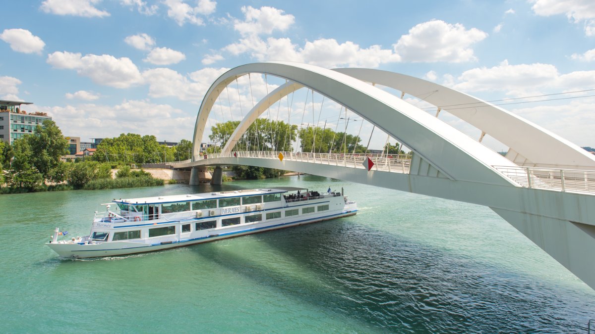 Un bateau des Bateaux Lyonnais naviguant sous une passerelle blanche à Lyon Un bateau des Bateaux Lyonnais naviguant sous une passerelle blanche à Lyon