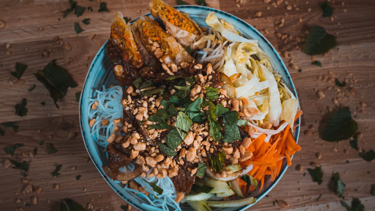Un bo bun garni de nems, vermicelles, cacahuètes, carottes et herbes fraîches dans un bol bleu chez Battam Asian Food à Lyon