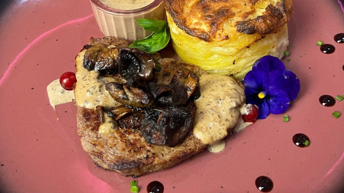 Un pavé de viande sauce champignons et son gratin sur une assiette rose, chez Bloomy Coffee à Lyon