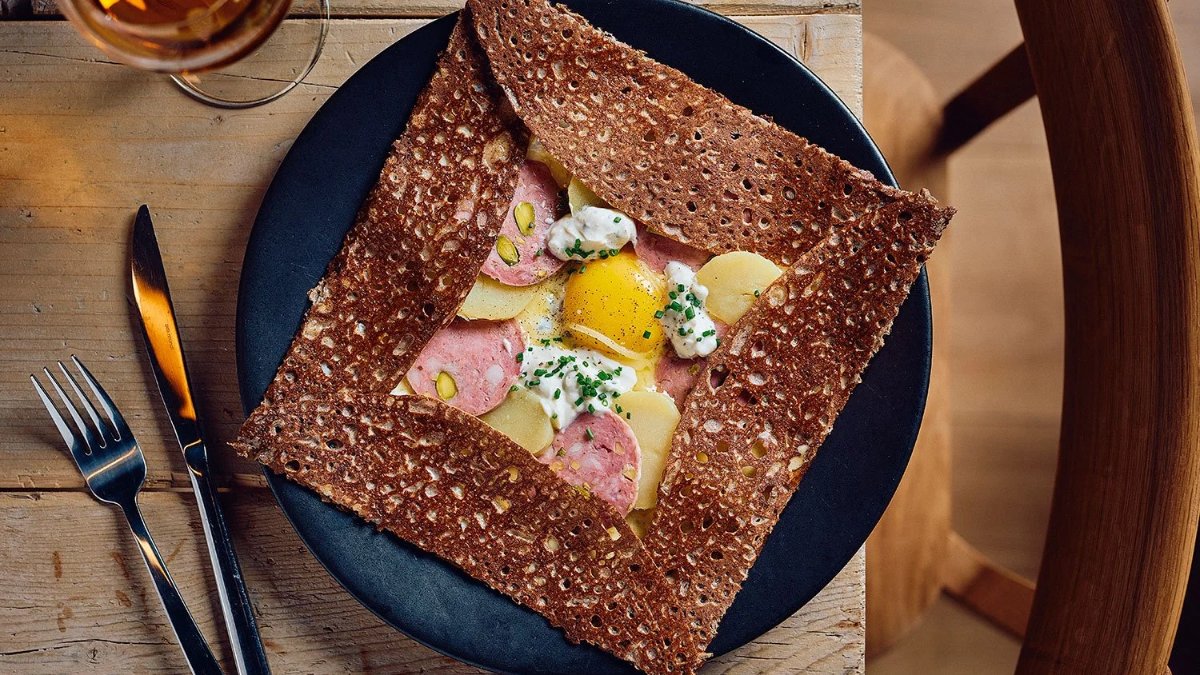 Une galette bretonne carrée au saucisson, œuf et fromage frais, servie dans une assiette noire chez Breizh Café Lyon Albon Une galette bretonne carrée au saucisson, œuf et fromage frais, servie dans une assiette noire chez Breizh Café Lyon Albon