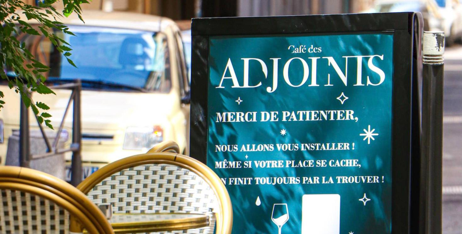 L’ardoise « Café des Adjoints » posée devant les chaises de la terrasse, à Lyon L’ardoise « Café des Adjoints » posée devant les chaises de la terrasse, à Lyon
