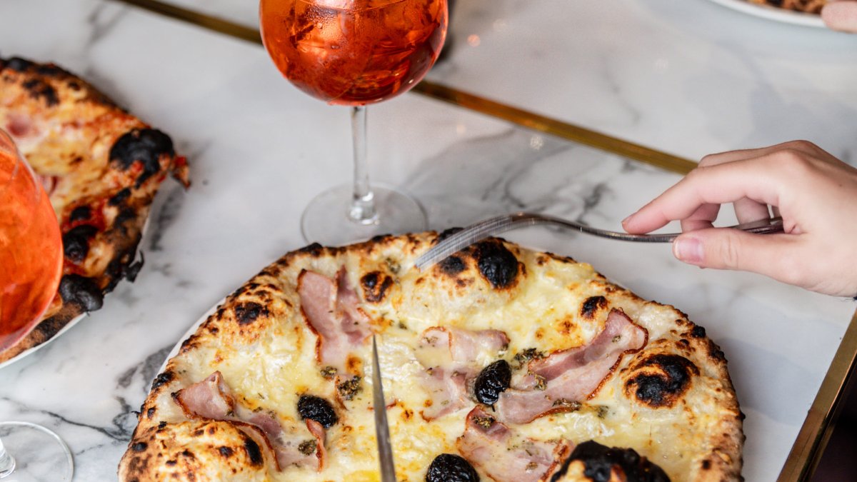 Une pizza au jambon cuite au feu de bois, découpée à table, avec un spritz, chez Carlo Gerland à Lyon Une pizza au jambon cuite au feu de bois, découpée à table, avec un spritz, chez Carlo Gerland à Lyon