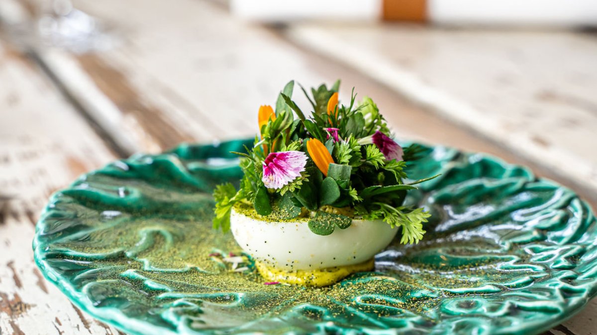 Un plat aux fleurs comestibles dressé sur une assiette verte en feuille de chou, chez Chez Pimousse à Lyon
