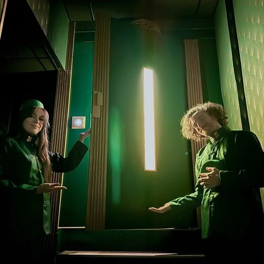 Deux personnages en uniforme vert de groom dans l’ascenseur de la salle L’Hôtel des Ombres d’Enigmatic Live Escape Game Lyon