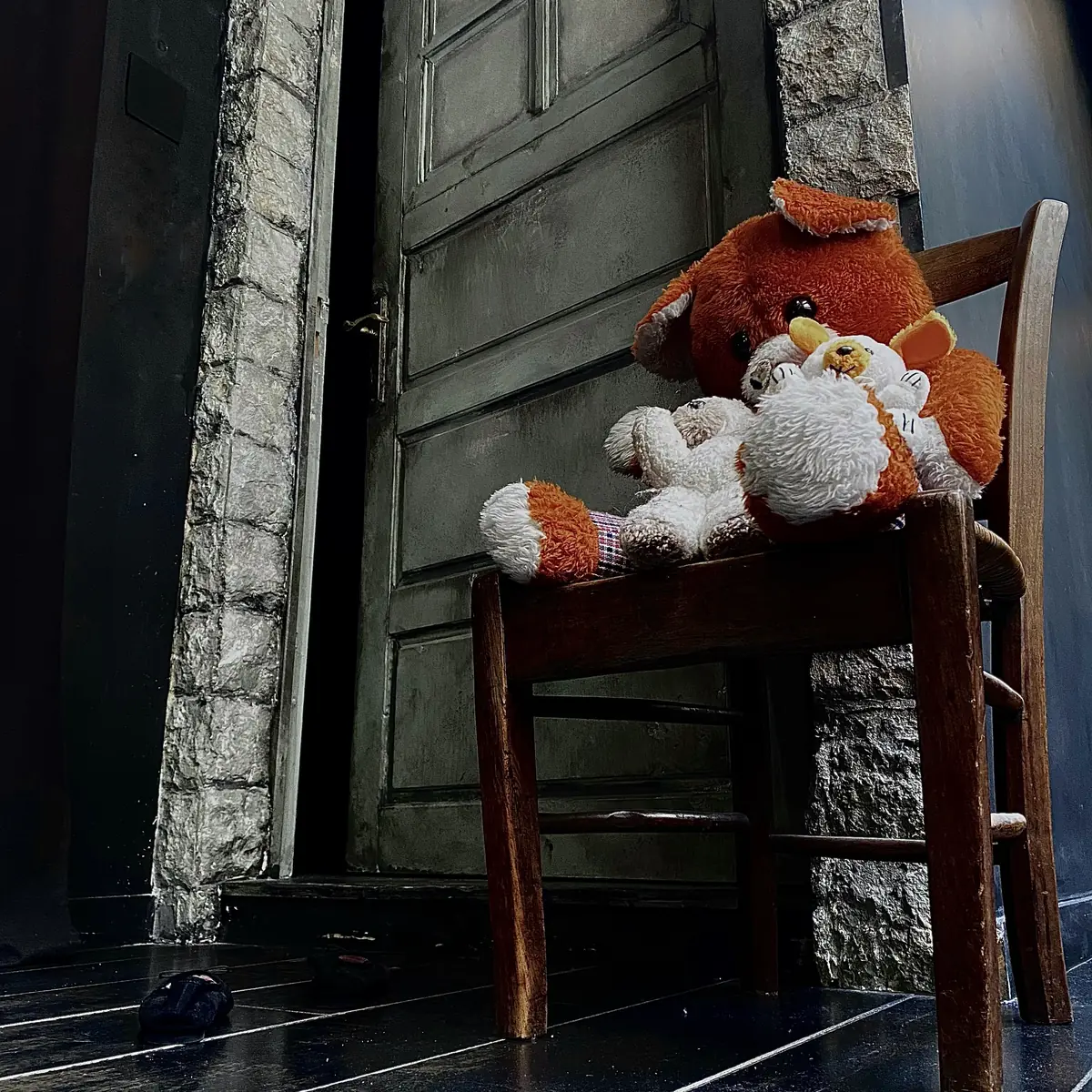 Enigmatic Live Escape Game Lyon – salle L’Orphelinat Une chaise en bois portant deux peluches abîmées devant une porte ancienne, dans la salle L’Orphelinat d’Enigmatic Live Escape Game Lyon