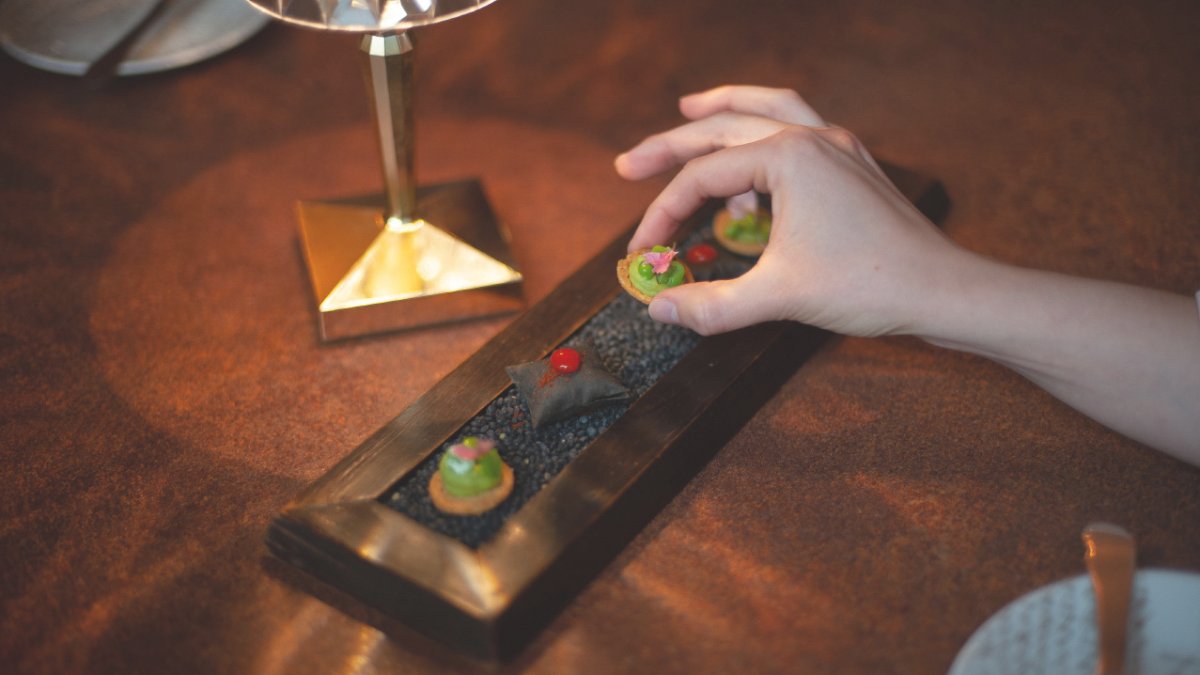 Des amuse-bouches posés sur une planche en bois, dont l’un est saisi du bout des doigts, à la table de L’Alexandrin, restaurant de Laurent Rigal à Lyon Des amuse-bouches posés sur une planche en bois, dont l’un est saisi du bout des doigts, à la table de L’Alexandrin, restaurant de Laurent Rigal à Lyon