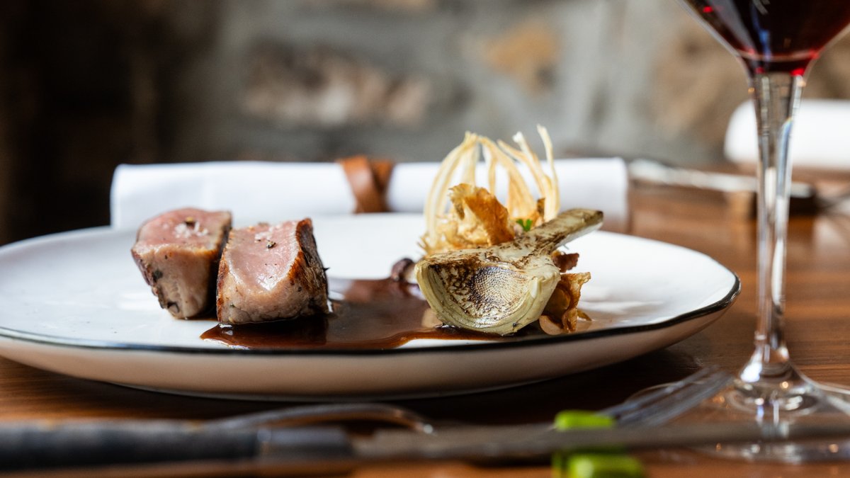 Une assiette de viande et sa garniture raffinée, avec un verre de vin rouge, à L’Art & la Manière à Lyon