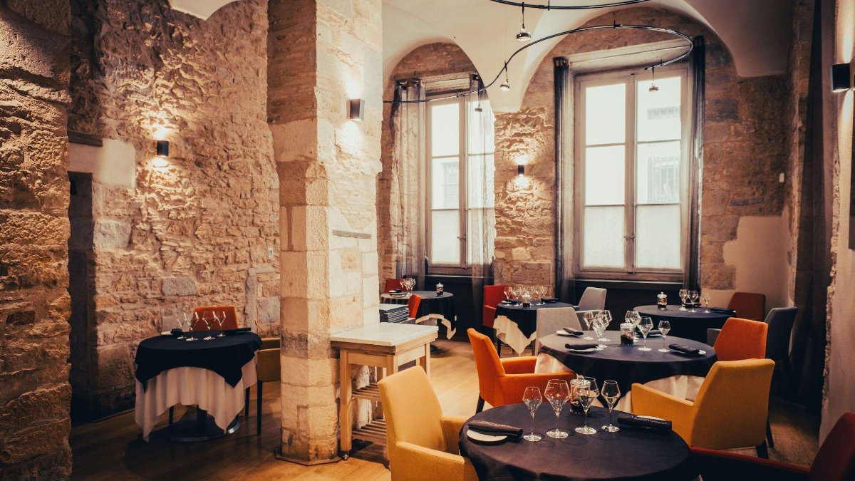 La salle voûtée en pierre de La Quintessence, avec ses fauteuils orange et ses grandes fenêtres, à Lyon