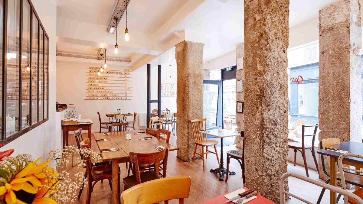 Une salle lumineuse aux piliers de pierre, tables en bois et grandes baies vitrées au restaurant Le Desjeuneur à Lyon Une salle lumineuse aux piliers de pierre, tables en bois et grandes baies vitrées au restaurant Le Desjeuneur à Lyon