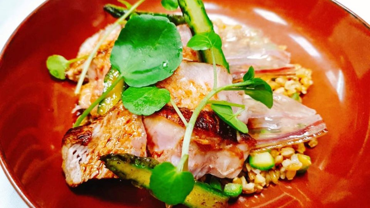 Un plat raffiné de poisson et d’asperges aux jeunes pousses, servi dans une assiette rouge au restaurant Le Tiroir à Lyon Un plat raffiné de poisson et d’asperges aux jeunes pousses, servi dans une assiette rouge au restaurant Le Tiroir à Lyon