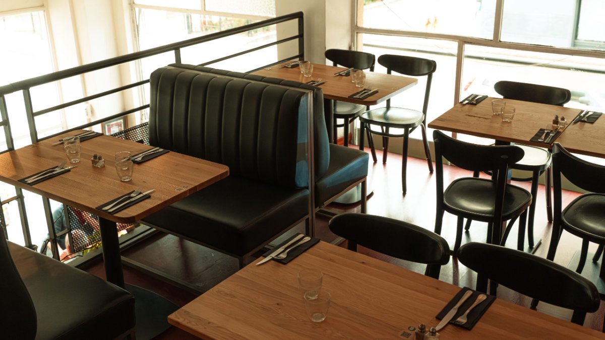 La salle des 3 Chauves à Lyon, avec ses banquettes en cuir noir, ses tables en bois et ses chaises bistrot près des grandes baies vitrées
