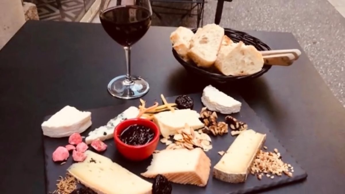Une planche de fromages et de charcuterie avec un verre de vin rouge et une corbeille de pain aux Fromagivores, bar à fromages à Lyon