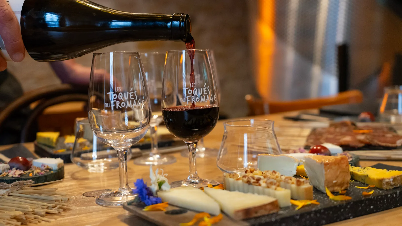 Vin rouge versé dans des verres Les Toqués du fromage, devant un plateau de fromages