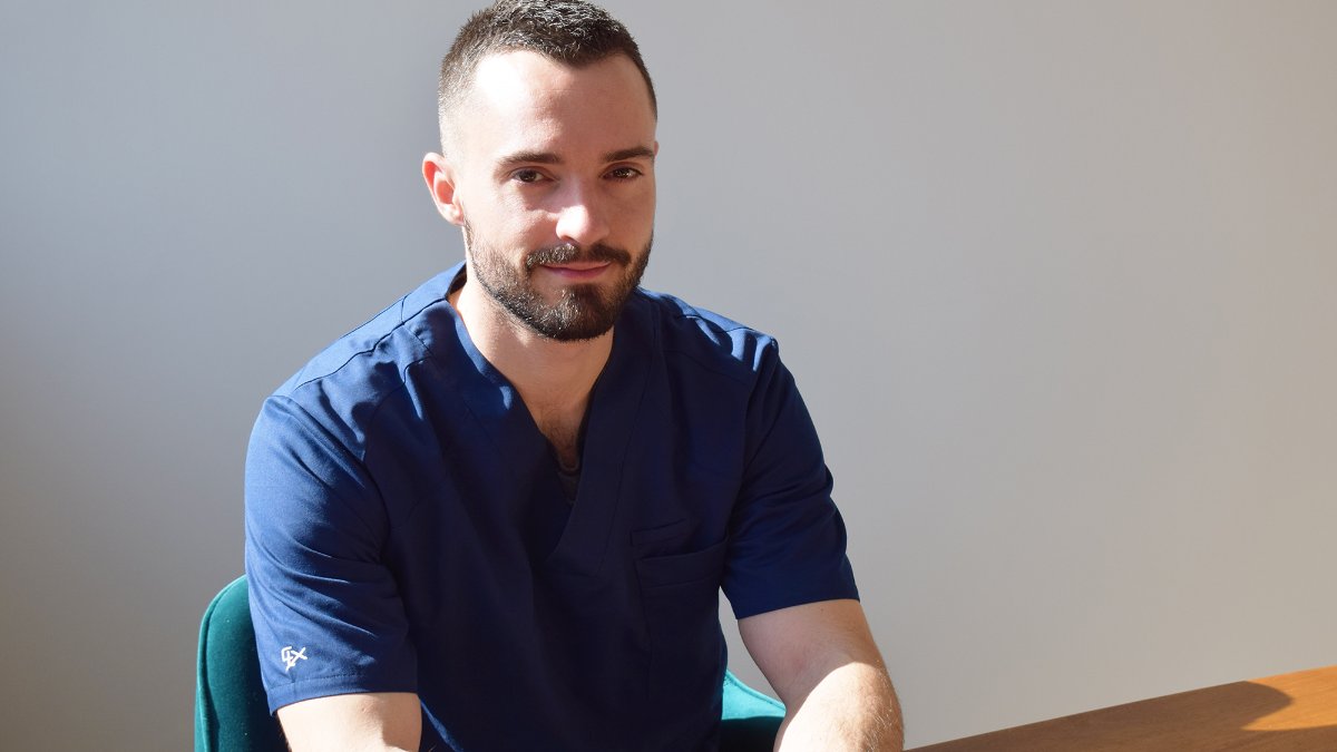 Loïc Rochand, ostéopathe à Lyon, en blouse bleue assis à son bureau au cabinet Loïc Rochand, ostéopathe à Lyon, en blouse bleue assis à son bureau au cabinet