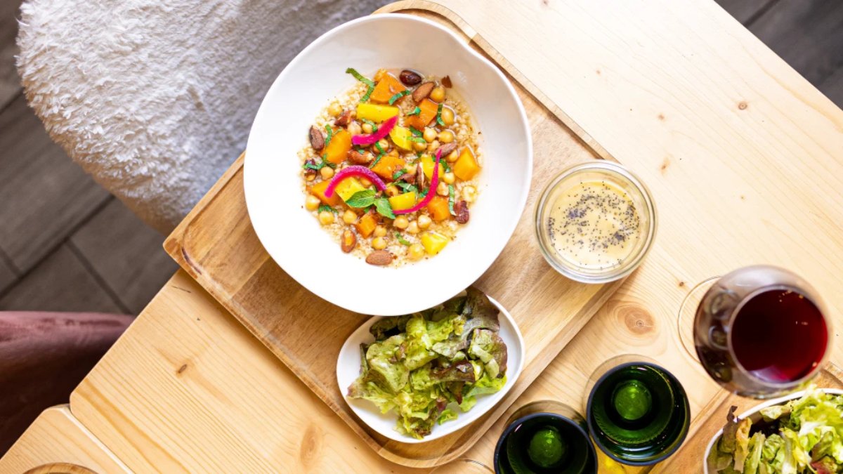 Un bol de légumes rôtis et de pois chiches posé sur un plateau en bois avec une salade verte et un verre de vin rouge chez Menthe Poivrée, restaurant et coffee-shop à Lyon