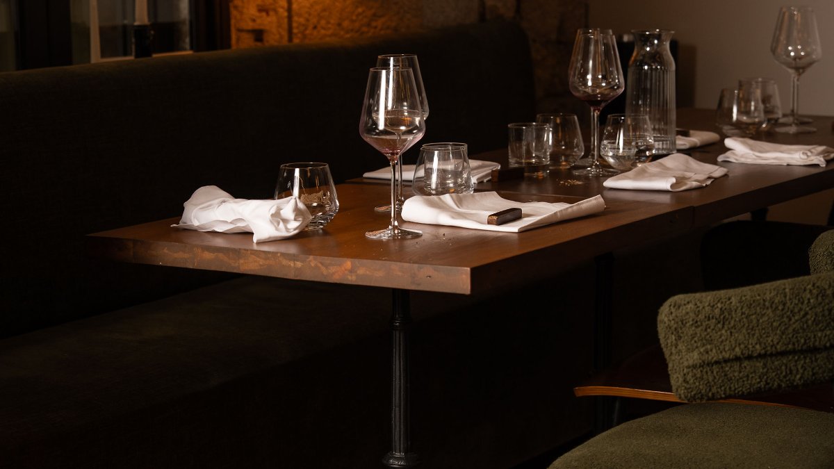 Une table en bois sertie de verres à vin, de carafes et de serviettes blanches dans la salle tamisée de Murmures, restaurant à Lyon