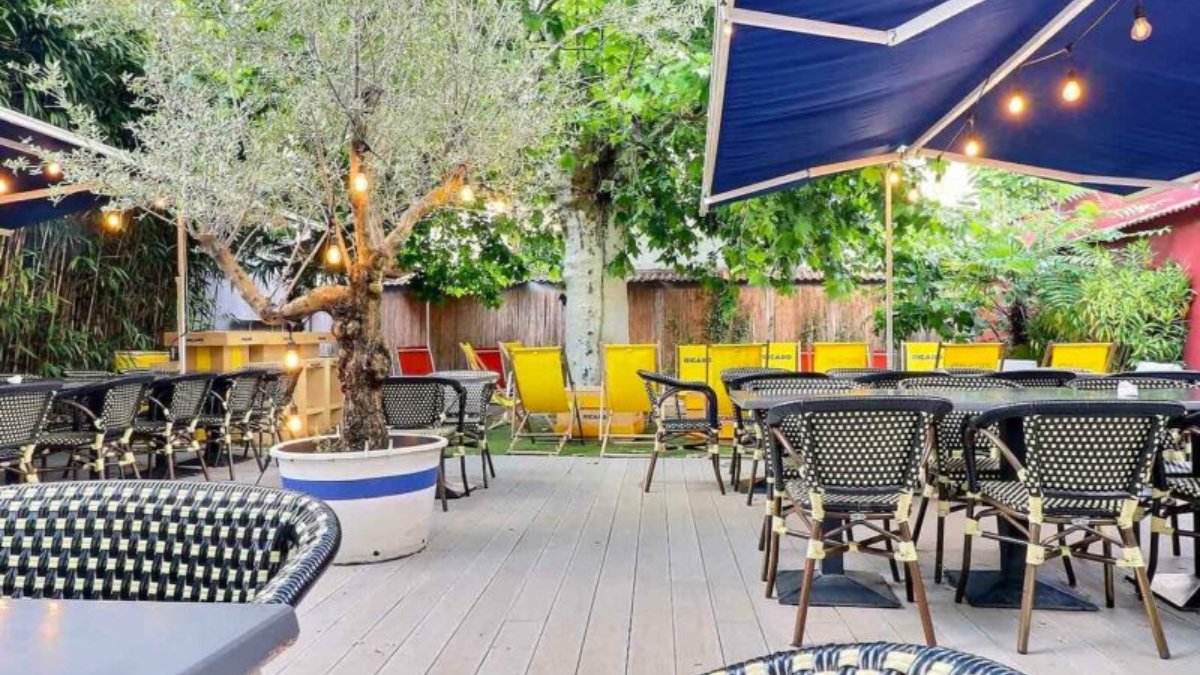 La terrasse ombragée d’O’Kypos à Lyon, avec ses fauteuils en rotin, ses chaises jaunes et son olivier en pot
