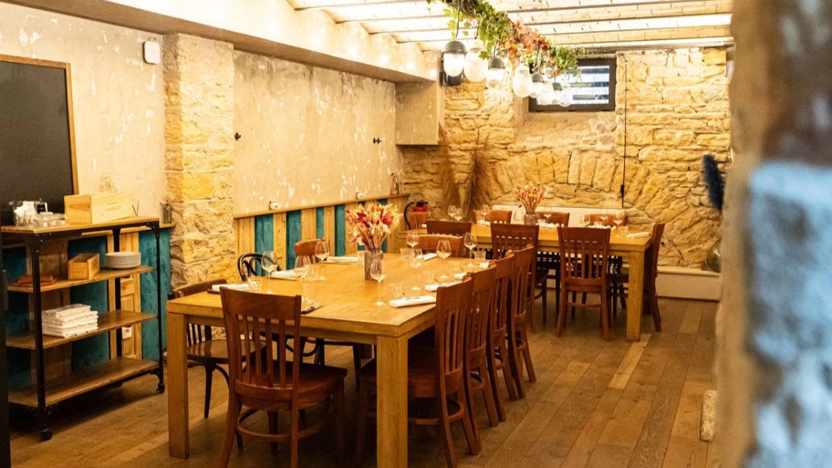 Une salle voûtée en pierre apparente chez Roliko, à Lyon, avec une grande table en bois et ses chaises en bois