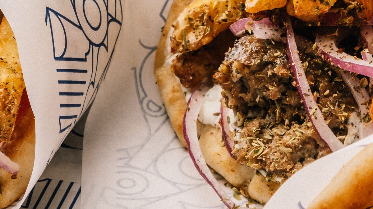 Un pita garni de viande grillée, d’oignons rouges et de sauce blanche, dans son papier imprimé, chez Skepsi, street food grecque à Lyon